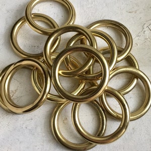 May include: A collection of shiny, golden-colored metal rings. The rings are circular with a smooth, polished surface. They are arranged in a slightly overlapping pattern, creating a visually appealing display. The rings appear to be made of brass or a similar material.
