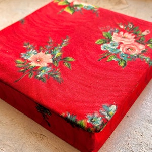 May include: A red fabric box with a floral pattern. The box is square shaped and covered in red fabric with a white floral design.