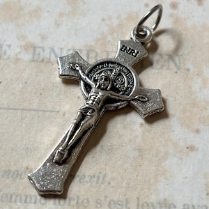 May include: Silver-toned crucifix pendant with a detailed depiction of Jesus Christ on the cross. The pendant features a circular medallion with the inscription "INRI" and a Saint Benedict medal.
