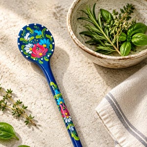 Può includere: Un lungo cucchiaio in legno blu scuro con motivi floreali dipinti a mano in tonalità vivaci di rosa, azzurro, bianco e verde. L'intricato motivo botanico in stile popolare si estende dalla parte concava del cucchiaio lungo tutto il manico.