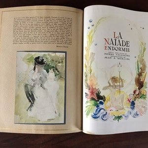 May include: An open book with a watercolor illustration of a woman and a child on the left page. The right page features a watercolor illustration of a mermaid with a trident, surrounded by seaweed and coral. The title of the book is "La Naiade Endormie" with the author's name, Pierre Valmig&egrave;re, and the illustrator's name, Jean A. Mercier.