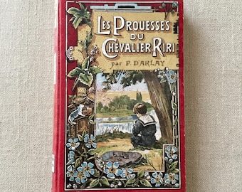May include: A vintage hardcover book titled Les Prouesses du Chevalier Riri by P. Darlay. The red cover features a central illustration of a child in a sailor suit sitting by a river, framed by blue flowers, green leaves, and a cat.