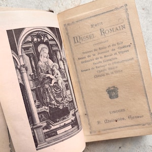 Puede incluir: Un libro vintage encuadernado en cuero de color beige titulado "Petit Missel Romain" con una ilustración en blanco y negro de la Virgen María y el niño Jesús en la página izquierda. El libro contiene oraciones, misas y otros textos litúrgicos.