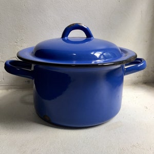 Op de afbeelding: Een blauwe emaille pan met een deksel en twee handvatten. De pan heeft een zwarte rand rond de bovenkant.