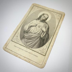 Puede incluir: Tarjeta religiosa antigua con una ilustración en blanco y negro de Jesús, con un halo, señalando su corazón. La tarjeta tiene bordes decorativos y texto en francés. Tarjeta rectangular con esquinas redondeadas.