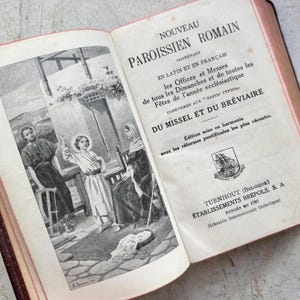 May include: A vintage book titled "Nouveau Paroissien Romain" with a black and white illustration of a family on the cover. The book contains text in French and Latin.