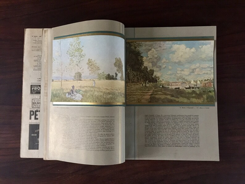 May include: An open book with two paintings of landscapes. The left page shows a painting of a field with trees and a couple sitting on a blanket. The right page shows a painting of a river with trees and a town in the distance.