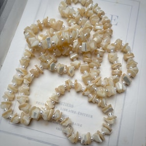 May include: Several necklaces and bracelets crafted from irregular, pale shell fragments and small, round white pearls. The jewellery is displayed on a vintage book page, offering a soft, neutral colour scheme.