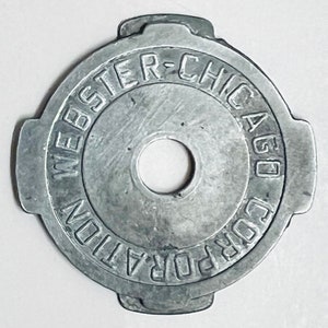 May include: A silver metal token with the text "WEBSTER-CHICAGO CORPORATION" around the edge.