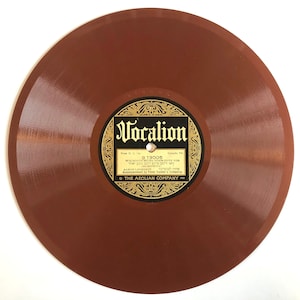 May include: A brown vinyl record with a gold label that reads "Vocalion" and "B 13005". The label also includes the text "Wie Senen Meine Bien Cute Yor" and "וואו זיינען מיינע זיבען מומע אחר" in Hebrew. The label also includes the text "Aaron Leuedkfy" and "אחרן לעבעדעד" in Hebrew. The label also includes the text "Accompaniment d'hestra" and "THE AEOLIAN COMPANY".