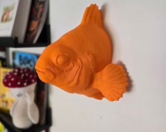 May include: Orange 3D printed fish wall decor. The fish has a detailed texture and a realistic shape.