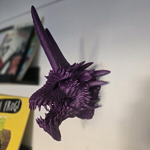 May include: Purple 3D printed dragon head wall mount. The dragon has a long, pointed horn and an open mouth with sharp teeth.