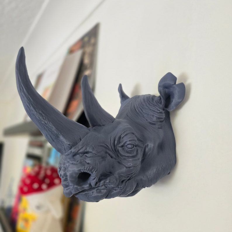 Peut inclure: Une t&ecirc;te de rhinoc&eacute;ros grise en guise de d&eacute;coration murale. La t&ecirc;te est d&eacute;taill&eacute;e avec une peau textur&eacute;e et une grande corne.