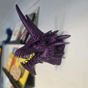 May include: Purple dragon head wall mount with a textured surface and sharp teeth. The dragon has a long, pointed horn on its head.