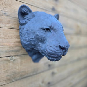 May include: A grey, realistic-looking sculpture of a panther head mounted on a wooden wall. The panther's eyes are closed and its mouth is slightly open.