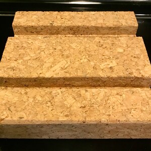 May include: A three-tiered cork stand with a natural brown color. The stand is made of compressed cork and has a rectangular shape.
