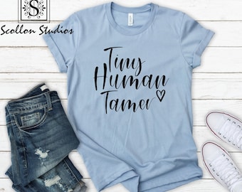 May include: A light blue t-shirt with the text "Tiny Human Tamer" in black lettering with a small heart symbol.