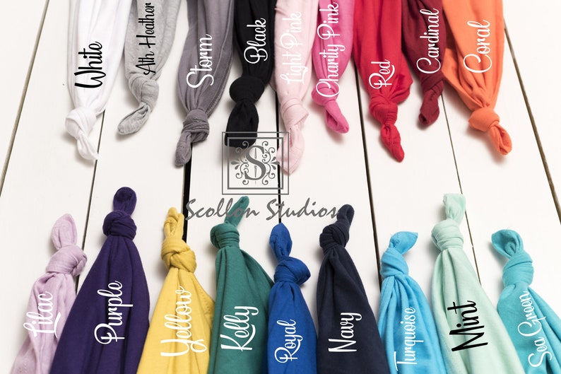 May include: A variety of t-shirt colors displayed on a white wooden surface. The colors include white, athletic heather, storm, black, light pink, charity pink, red, cardinal, coral, lilac, purple, yellow, kelly, royal, navy, turquoise, mint, and sea green.