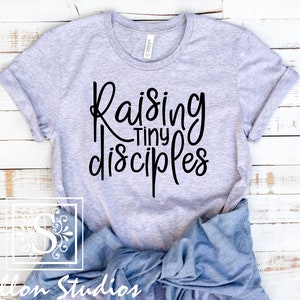 May include: A gray t-shirt with the text "Raising Tiny Disciples" in black lettering.