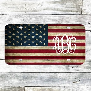 May include: A distressed American flag license plate with a white monogram in the center. The monogram is the letters "N.B.C." in a script font.