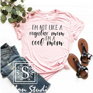 Op de afbeelding: Roze T-shirt met de tekst "I'm not like a regular mom I'm a cool mom" in zwarte cursieve letters.