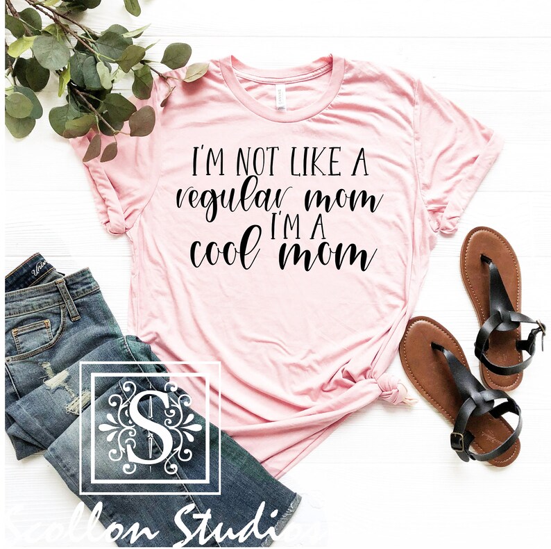 Op de afbeelding: Roze T-shirt met de tekst "I'm not like a regular mom I'm a cool mom" in zwarte cursieve letters.