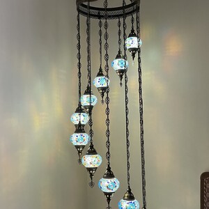 Op de afbeelding: Een Turkse kroonluchter met acht glazen bollen, elk met een mozaïekpatroon in tinten blauw, groen en geel. De kroonluchter is 86 inch hoog en 25 inch breed. Elke bol is 5 inch breed en 4 inch hoog.