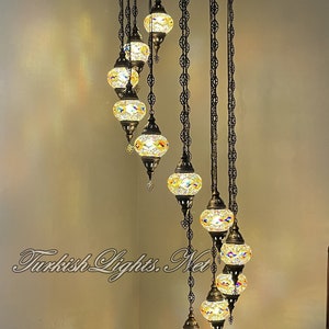 Op de afbeelding: Een spiraalvormige kroonluchter met acht kleurrijke glazen bollen die aan een zwart metalen frame hangen. De kroonluchter is 86 inch hoog en 25 inch breed. Elke bol is 5 inch breed en 4 inch hoog.