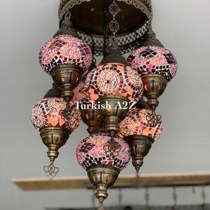 Op de afbeelding: Een hanglamp met meerdere mozaïek glazen kappen in oranje, rood en blauw. De lamp heeft een bronskleurig metalen frame en decoratieve accenten. De tekst "138-07" en "Turkish A2Z" zijn zichtbaar.
