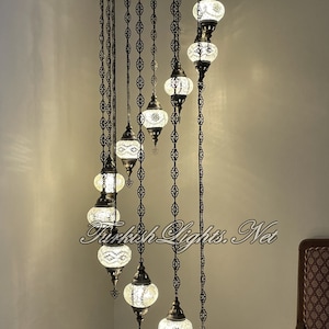 Op de afbeelding: Een witte glazen bol-kroonluchter met een zwart metalen frame en ketting. De kroonluchter is 86 inch hoog en 25 inch breed. Elke bol is 5 inch breed en 4 inch hoog. H11-20