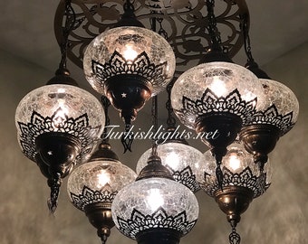 Puede incluir: Una lámpara de araña con seis globos de vidrio transparente con un acabado craquelado y una intrincada metalistería. Los globos están suspendidos de un marco circular de metal con un diseño decorativo. La lámpara de araña está iluminada con bombillas de luz blanca cálida.