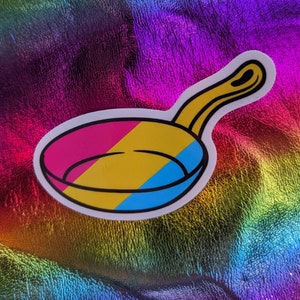 Może przedstawiać: Naklejka przedstawiająca patelnię z niebieskim, żółtym i różowym wzorem. Patelnia jest biała z czarnym obramowaniem.