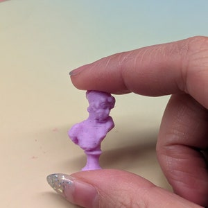 May include: A small, purple, 3D printed bust sculpture of a person. The sculpture is on a small base.