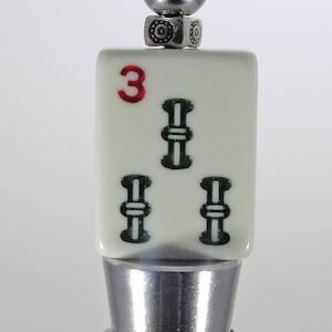 May include: A silver bottle stopper with a white ceramic top featuring a red number "3" and three green bamboo symbols.
