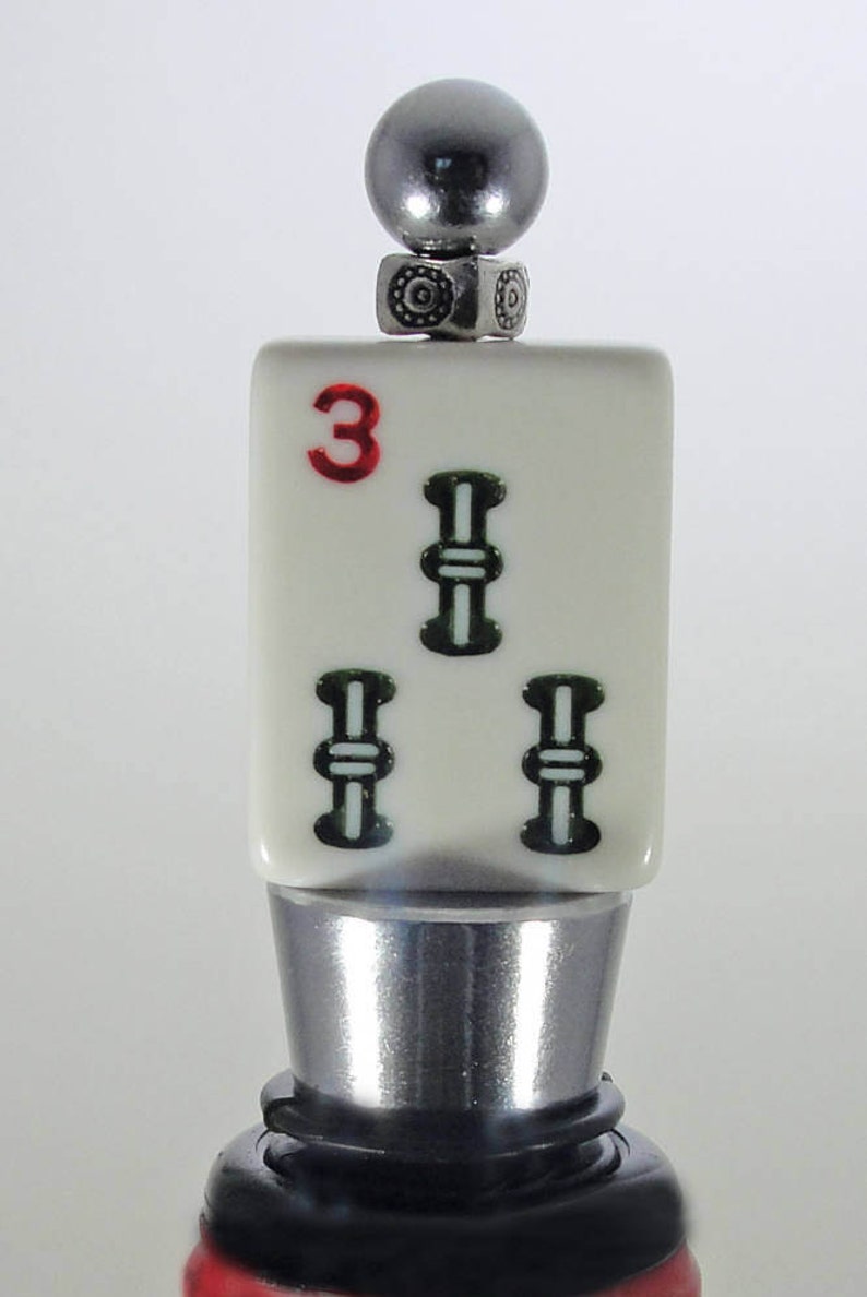 May include: A silver bottle stopper with a white ceramic top featuring a red number "3" and three green bamboo symbols.