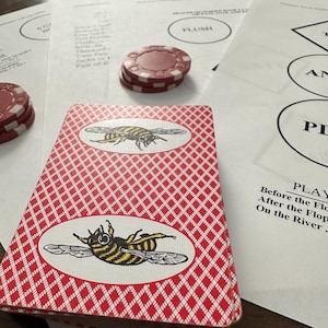 May include: A deck of playing cards with a red and white diamond pattern and a bee illustration. Poker chips in red and white are scattered around the cards and printed papers. The papers have text and circles.