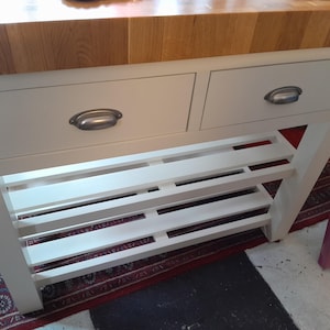 Puede incluir: Isla de cocina blanca con dos cajones y una estantería de listones. Los cajones tienen tiradores plateados. La encimera es de madera clara. La isla está sobre una alfombra estampada en rojo y negro.