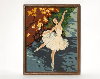 May include: A framed needlepoint picture of a ballerina in a white tutu dancing in a forest setting. The background features a blue and green water scene with a red and yellow tree.