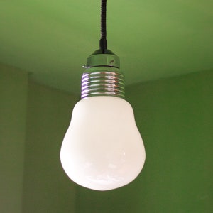 May include: A white light bulb hangs from a black cord and a silver ceiling fixture against a green wall.