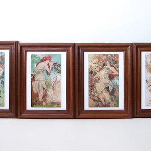 May include: Four framed art prints featuring Art Nouveau illustrations. Each print showcases a woman in flowing robes with floral and natural elements. The frames are a dark wood, and the prints have a vintage aesthetic.