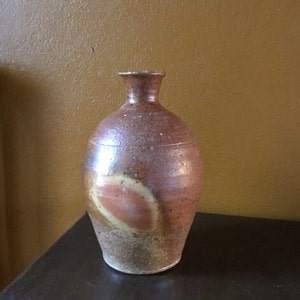 Peut inclure: Un vase en céramique brun avec un glaçage brun clair et orange. Le vase a un corps arrondi et un col étroit.