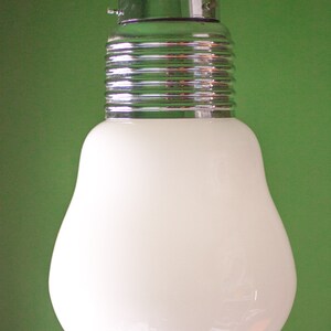 May include: A white glass light bulb with a chrome metal base and a black cord hanging from the ceiling.