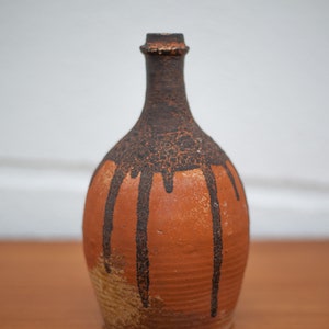 Peut inclure: Un vase en céramique brun avec un glaçage noir en gouttes. Le vase a un corps rond et un col étroit.