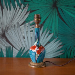 Op de afbeelding: Een blauwe en witte keramische tafellamp met een bloemenmotief en een messing voet. De lamp heeft een snoer en een stekker.