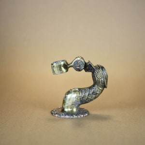 Puede incluir: Un soporte decorativo de latón con forma de pájaro con un diseño detallado. El soporte tiene una base redonda y un cuello curvo con una pequeña taza en el extremo.