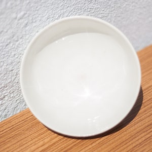 K&ouml;nnte beinhalten: Eine wei&szlig;e Keramiksch&uuml;ssel mit glatter, gl&auml;nzender Oberfl&auml;che. Die Sch&uuml;ssel ist leer und steht auf einer Holzoberfl&auml;che.