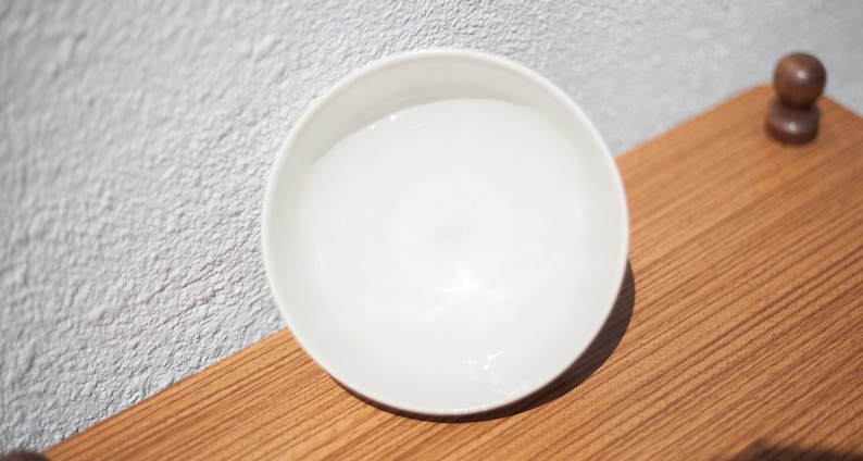 K&ouml;nnte beinhalten: Eine wei&szlig;e Keramiksch&uuml;ssel mit glatter, gl&auml;nzender Oberfl&auml;che. Die Sch&uuml;ssel ist leer und steht auf einer Holzoberfl&auml;che.