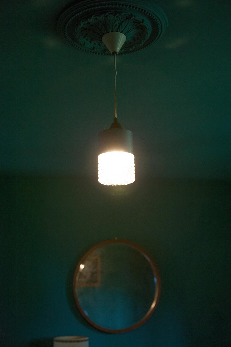K&ouml;nnte beinhalten: Eine wei&szlig;e Deckenleuchte mit einem dekorativen Blumendesign h&auml;ngt von der Decke. Ein wei&szlig;es Kabel verbindet die Leuchte mit einer mattierten Gl&uuml;hbirne.