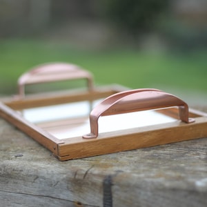 Puede incluir: Una bandeja de madera con asas de cobre. La bandeja tiene una superficie de espejo y es perfecta para servir aperitivos o bebidas.