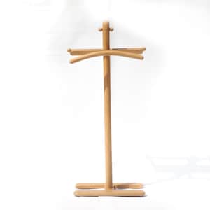 May include: A light-colored wooden valet stand featuring a central vertical post, a curved hanger bar at the top for garments, and a flat, horizontal base. The structure includes small rounded finials at the top and side connection points.